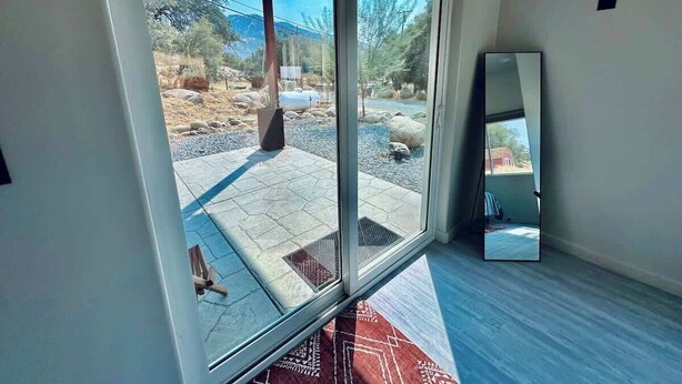 A room with a large sliding glass door leading to an outdoor patio with a stone floor and a view of a mountainous landscape. - Sequoia Retreat: BBQ, Patio, Near National Park (Three Rivers)