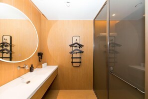 A modern bathroom with wooden walls, a white sink, a mirror, and a glass shower enclosure. - Ji Hotel (hangzhou West Lake Hubin Pedestrian Stre (Hangzhou)