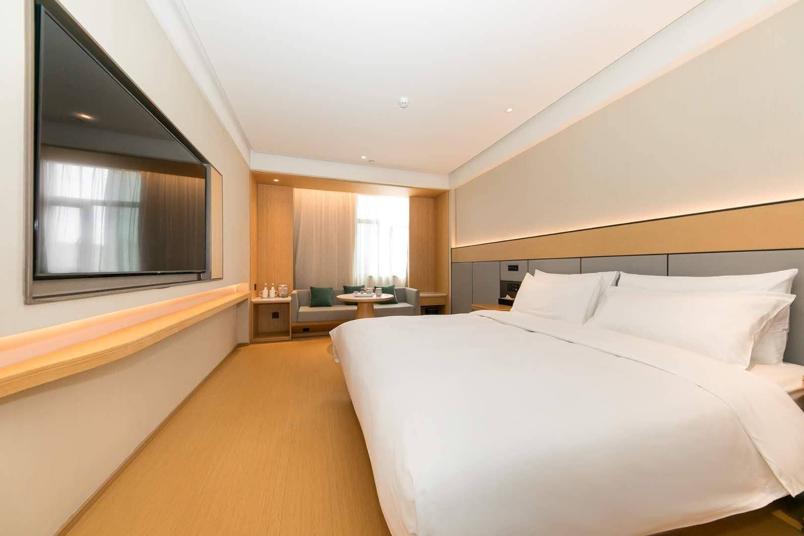 Habitació d'hotel amb un llit gran, una taula de nit, un televisor penjat a la paret i una finestra amb cortines.