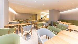 A modern dining area with tables and chairs, a kitchen area, and a seating area with a green upholstered bench. - Ji Hotel (hangzhou West Lake Hubin Pedestrian Stre (Hangzhou)