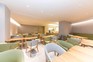 A modern dining area with tables and chairs, a kitchen area, and a seating area with a green upholstered bench. - Ji Hotel (hangzhou West Lake Hubin Pedestrian Stre (Hangzhou)