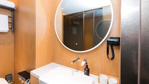 A modern bathroom with a round mirror, a white sink, a handheld showerhead, and a towel rack. - Ji Hotel (hangzhou West Lake Hubin Pedestrian Stre (Hangzhou)
