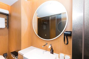 A modern bathroom with a round mirror, a white sink, a handheld showerhead, and a towel rack. - Ji Hotel (hangzhou West Lake Hubin Pedestrian Stre (Hangzhou)