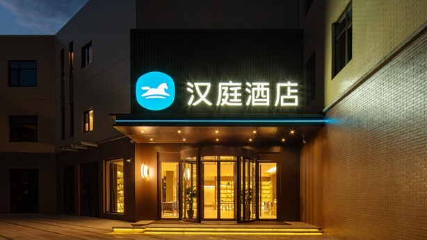 A hotel entrance with a revolving door, illuminated signage, and a brick facade. - Hanting Hotel (xianyang International Airport Hote (Xianyang)