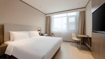A hotel room with a large bed, a desk, a chair, a TV, and a window with curtains.