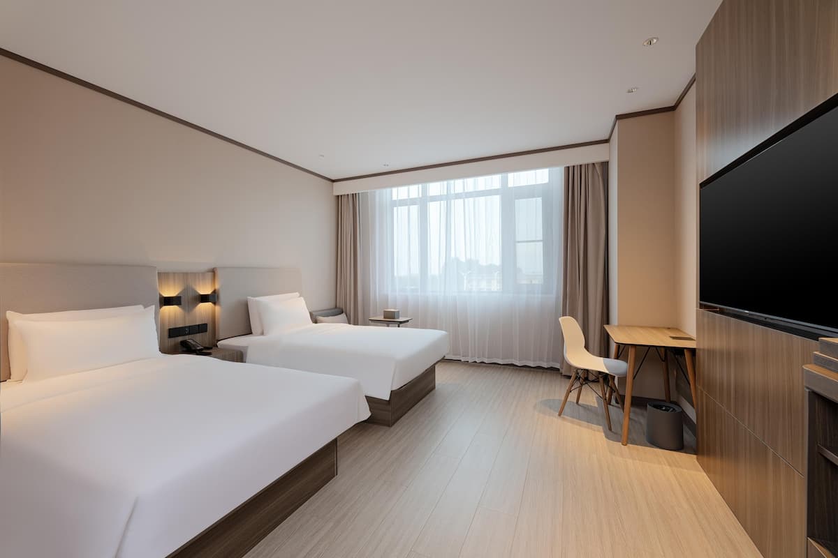 A hotel room with two beds, a TV, a desk, and a chair.