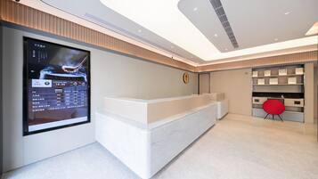 A modern hotel reception area with a digital display, a reception desk, and a red chair.