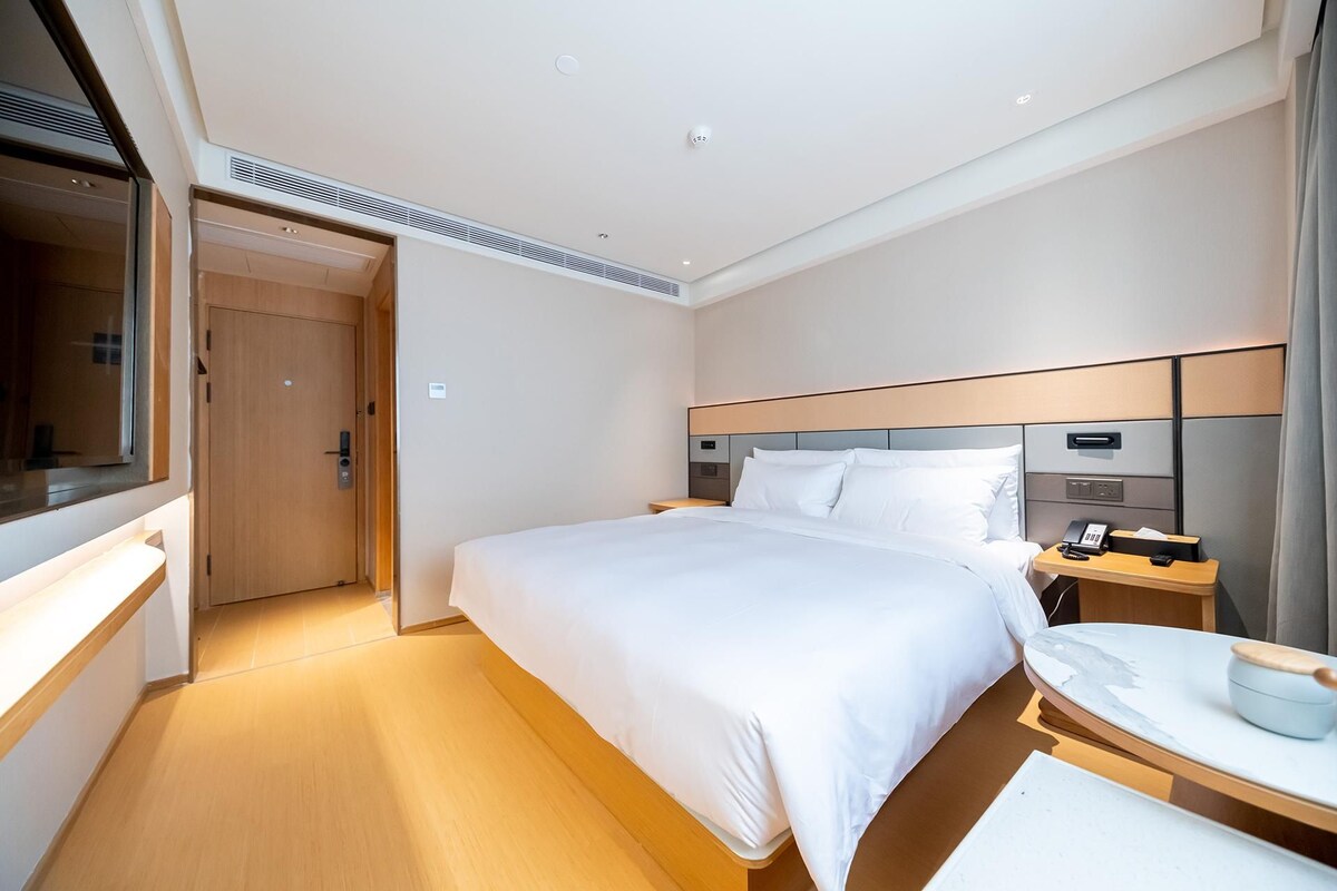 A modern hotel room with a large bed, bedside tables, a desk, and a mirror.