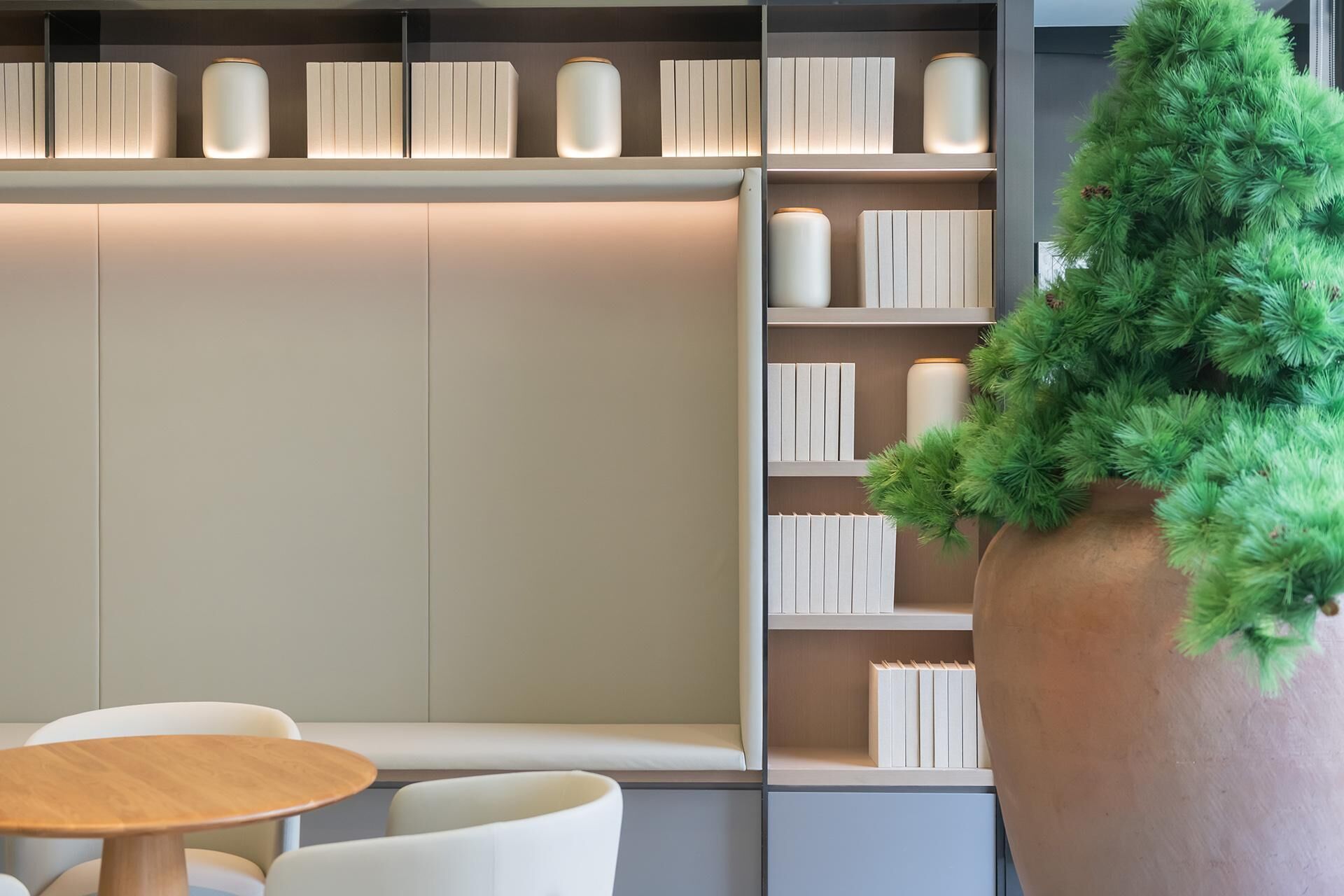 Um interior moderno com uma estante, uma mesa de madeira redonda e uma grande planta em vaso.