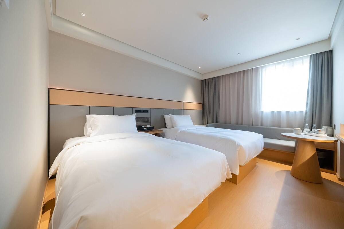 A hotel room with two beds, a desk, and a window with curtains.