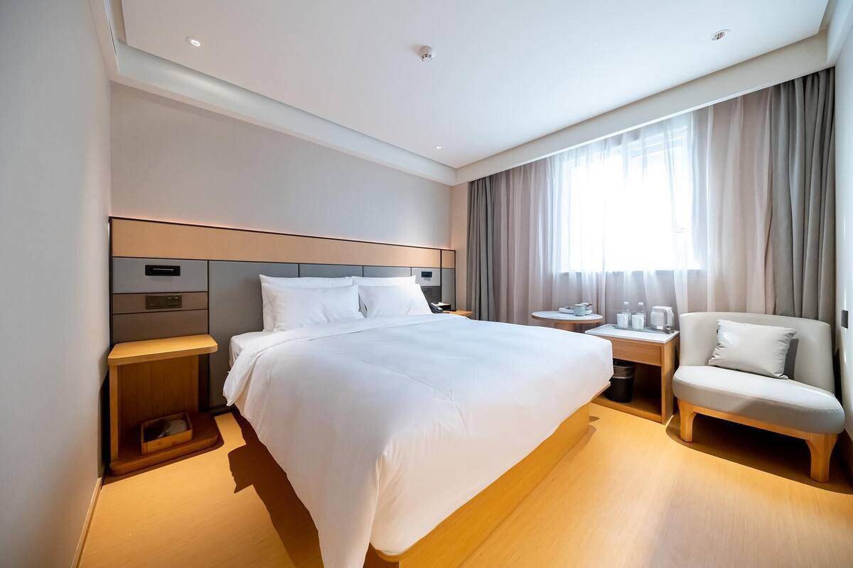 A hotel room with a large bed, bedside tables, a chair, and a window with curtains.