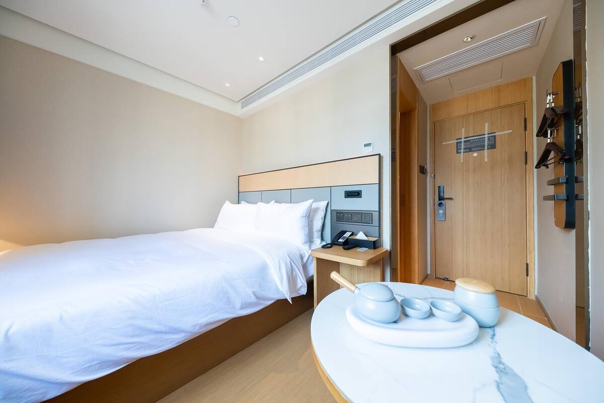 A hotel room with a bed, bedside table, and a small table with bowls and a teapot.