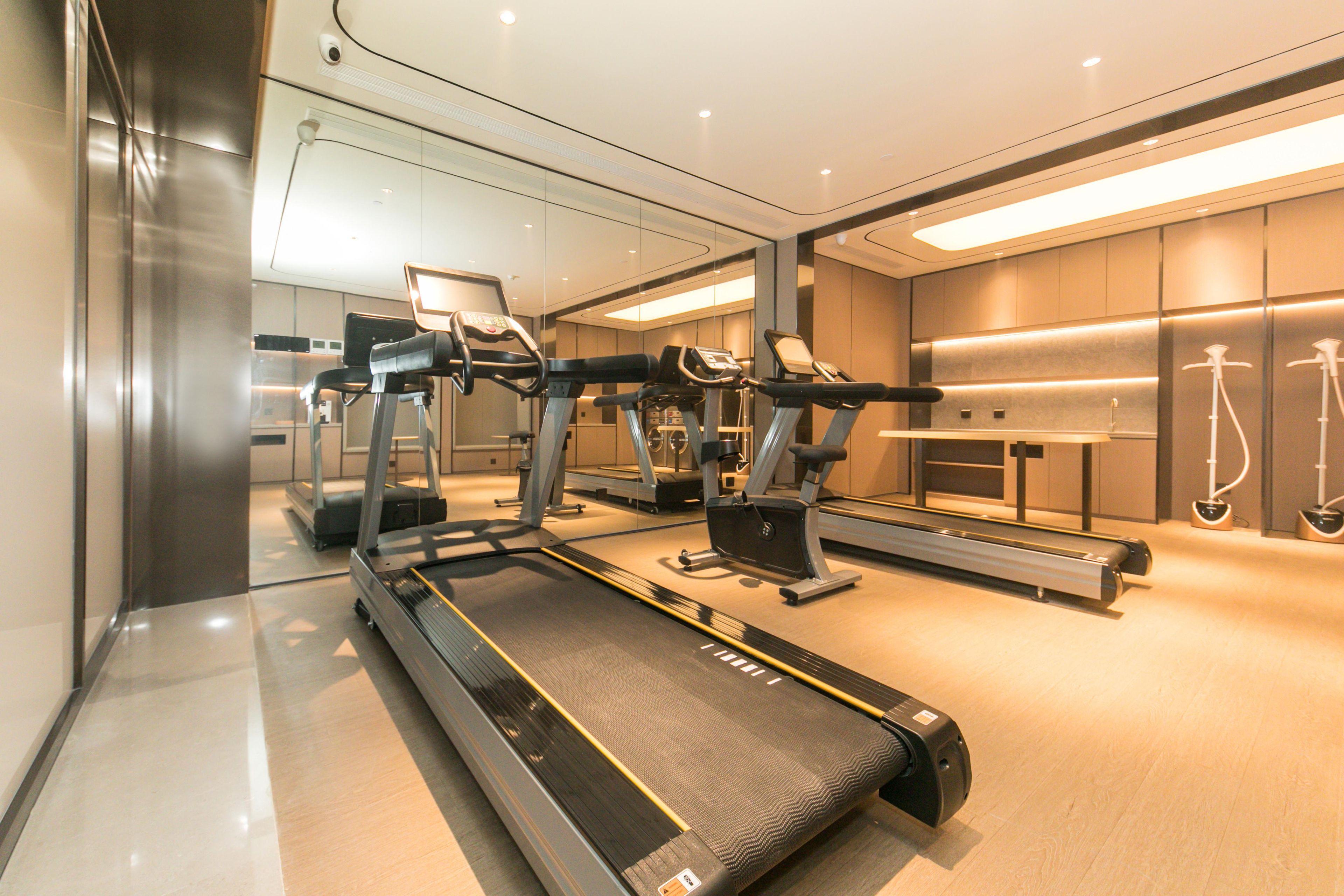 Un gimnasio moderno con cintas de correr, máquinas elípticas y un espejo grande.