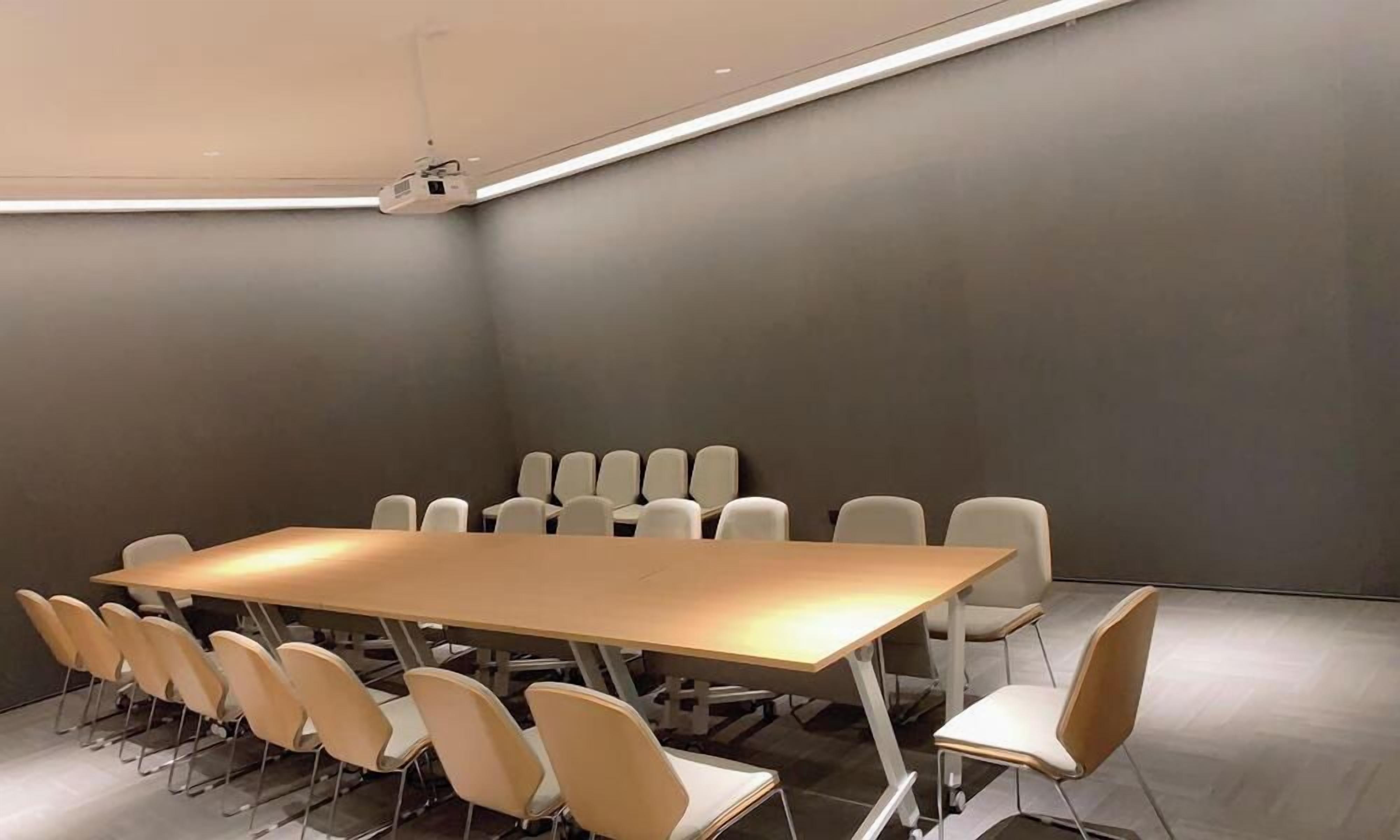Una sala de conferencias con una larga mesa y varias sillas, equipada con un proyector.