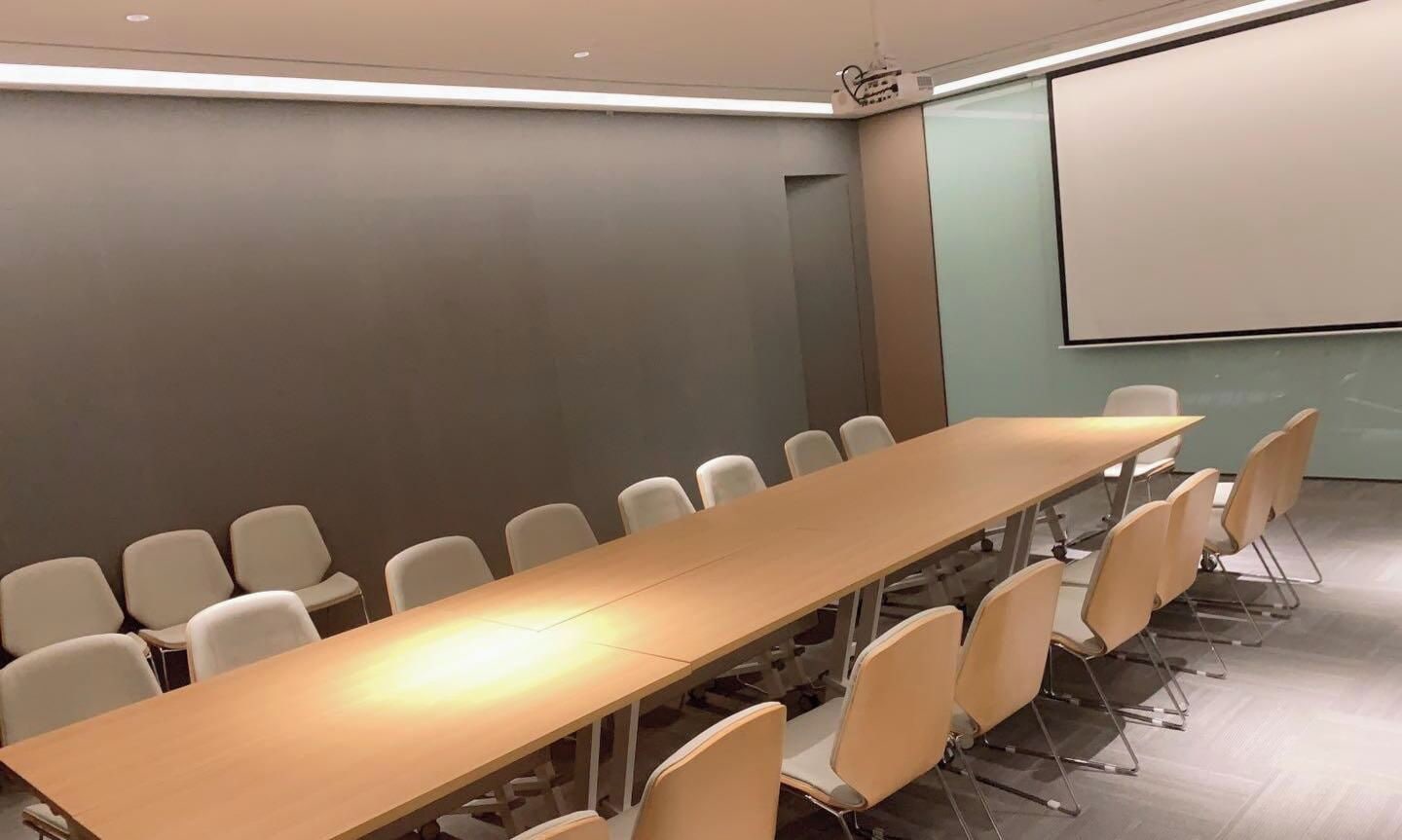 Un salón de conferencias con una larga mesa y sillas, una pantalla de proyector y una pizarra.