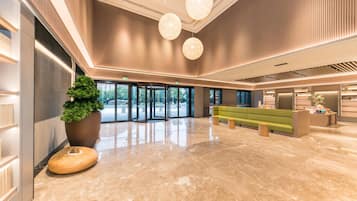 Un moderno vestíbulo con un sofá verde, una planta grande en maceta y un mostrador de recepción.