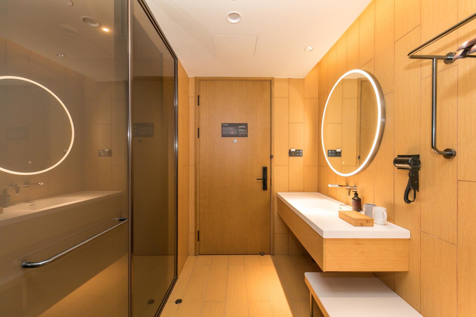 A modern bathroom with a glass shower enclosure, a vanity with a mirror, and a hairdryer on the wall.