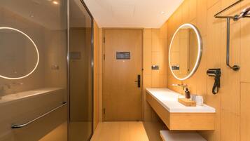 A modern bathroom with a glass shower enclosure, a vanity with a mirror, and a hairdryer on the wall.