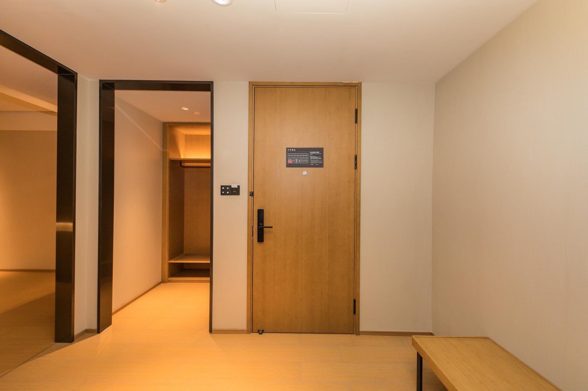 A hallway with a wooden door, a bench, and a light switch on the wall.
