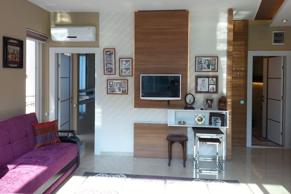 Una sala de estar moderna con un sofá, un televisor, una mesita y una zona de cocina con refrigerador y microondas.
