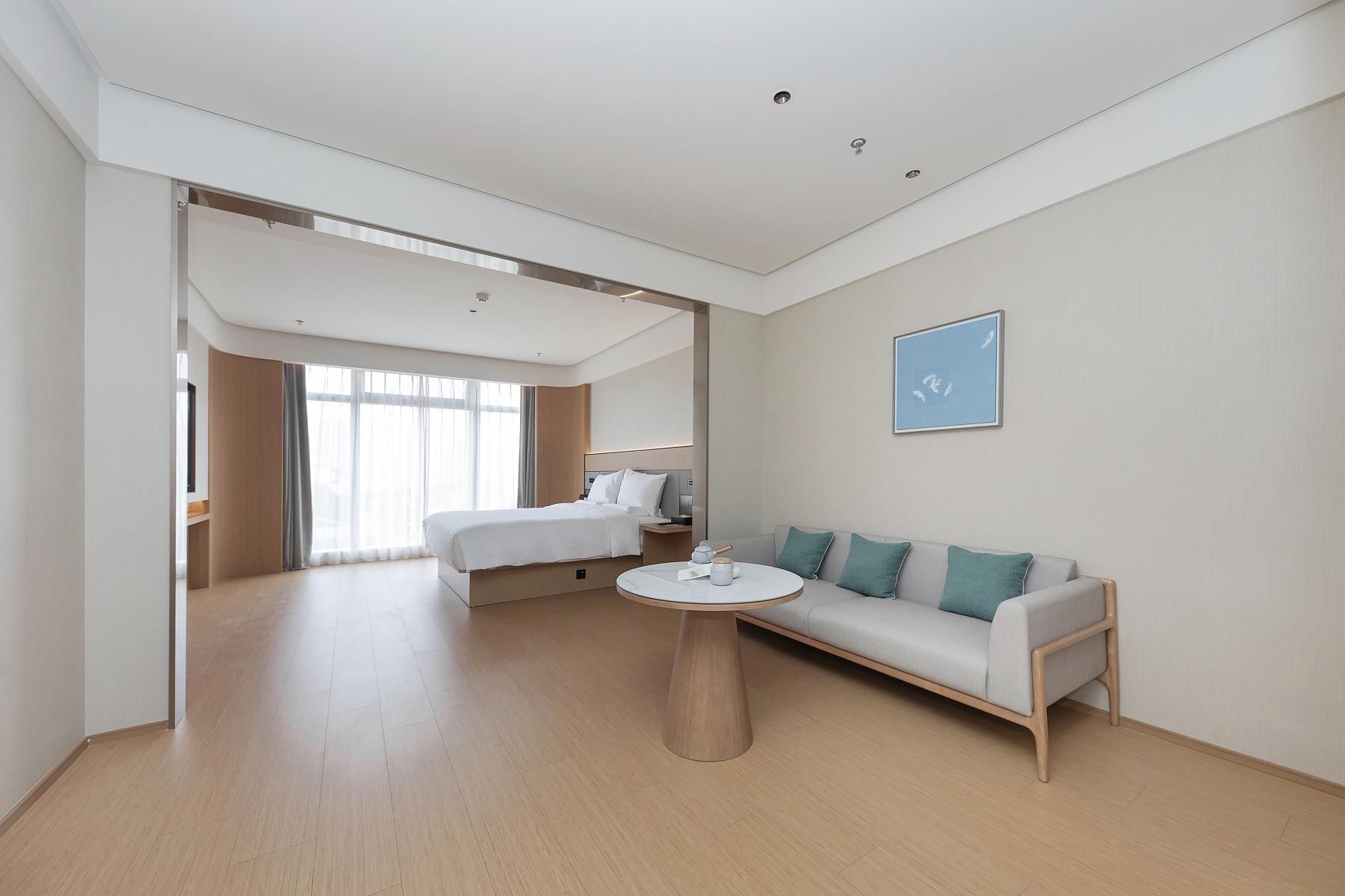 Una habitación de hotel moderna con cama, sofá, una mesa redonda y un ventanal grande.