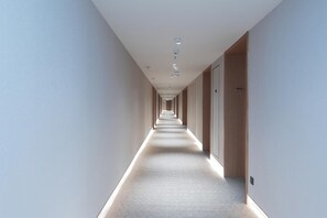 Un long couloir étroit, doté d’un sol recouvert de moquette, d’un éclairage encastré et de portes de part et d’autre.