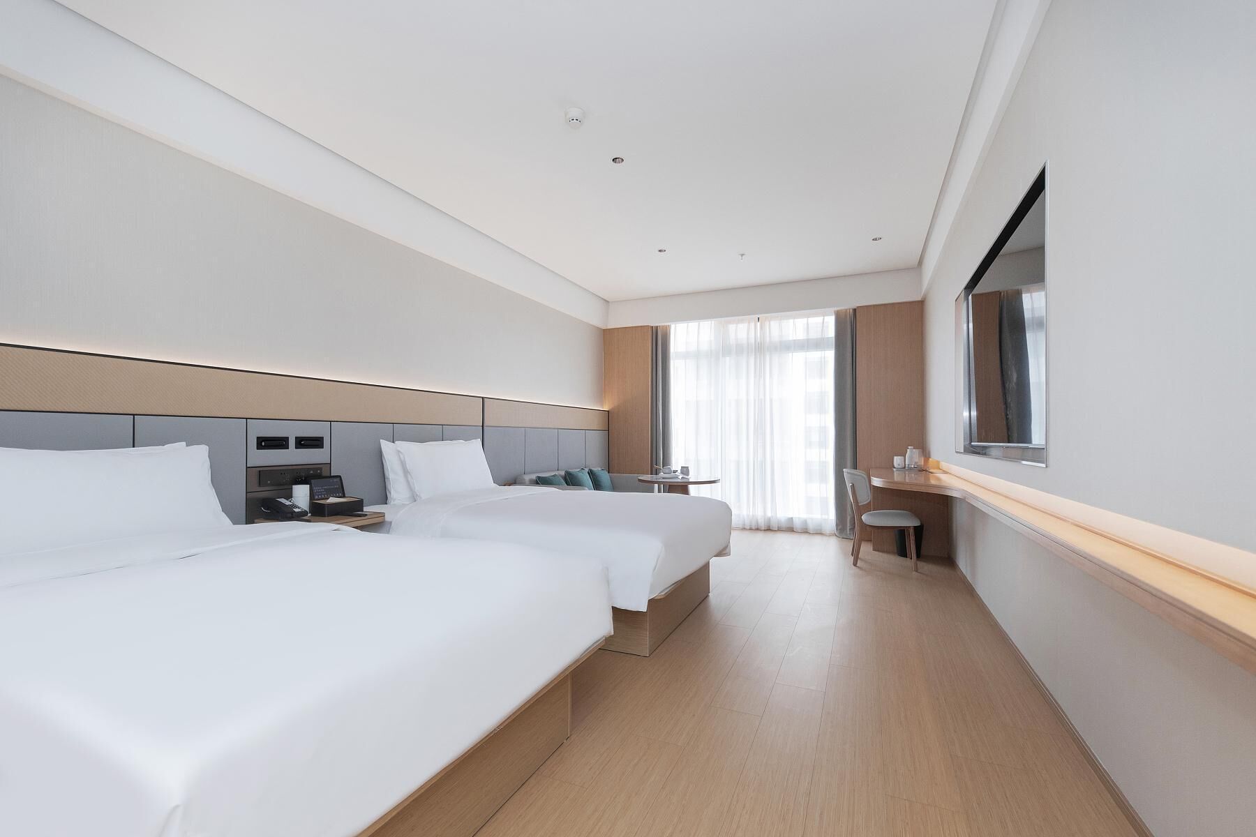 A hotel room with two beds, a desk, a chair, a small table, and a window with curtains.