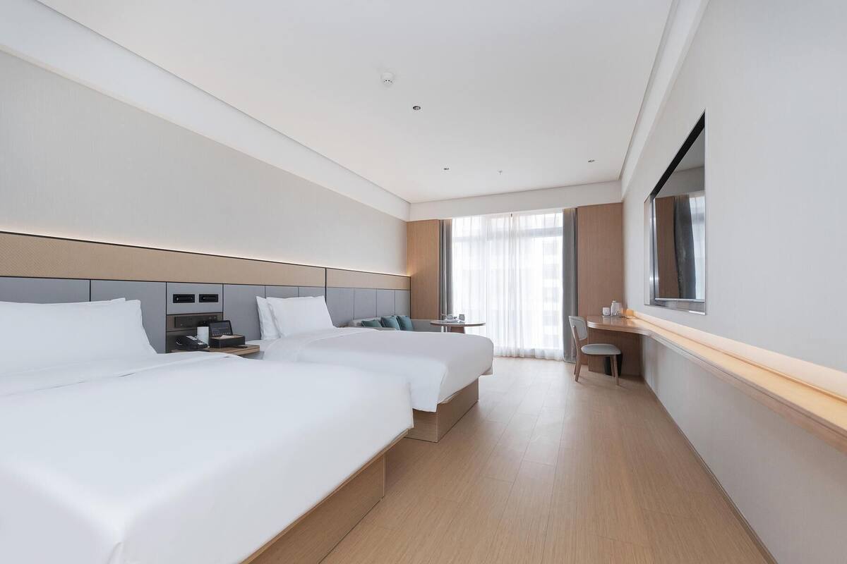 A hotel room with two beds, a desk, a chair, a small table, and a window with curtains.