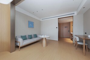 Une chambre d’hôtel moderne avec un canapé, une table de salle à manger ronde et un petit coin cuisine.