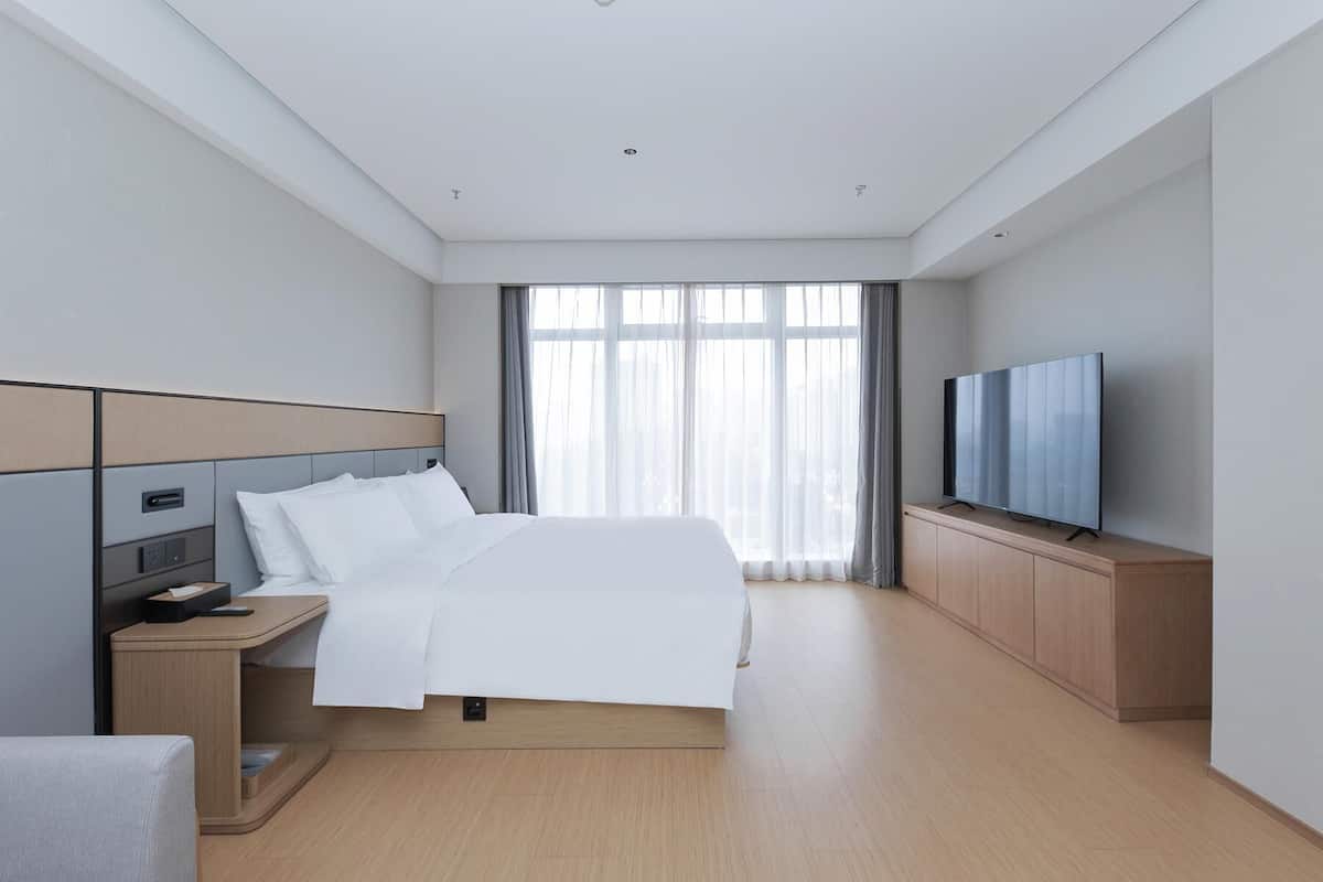 Et moderne hotelværelse med seng, natbord, fjernsyn og et stort vindue med gardiner.