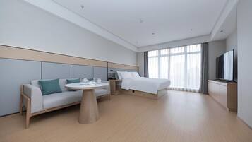 A modern hotel room with a bed, sofa, bedside table, and a TV.