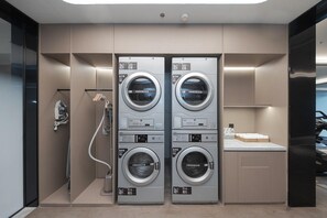 Une buanderie d’hôtel équipée de deux machines à laver et deux sèche-linge à chargement frontal, d’un porte-serviettes et d’un petit comptoir avec des bouteilles d’eau.