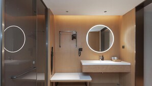 A modern bathroom with a glass shower enclosure, a vanity with a mirror, and a bench. - Ji Hotel (Wuhan)