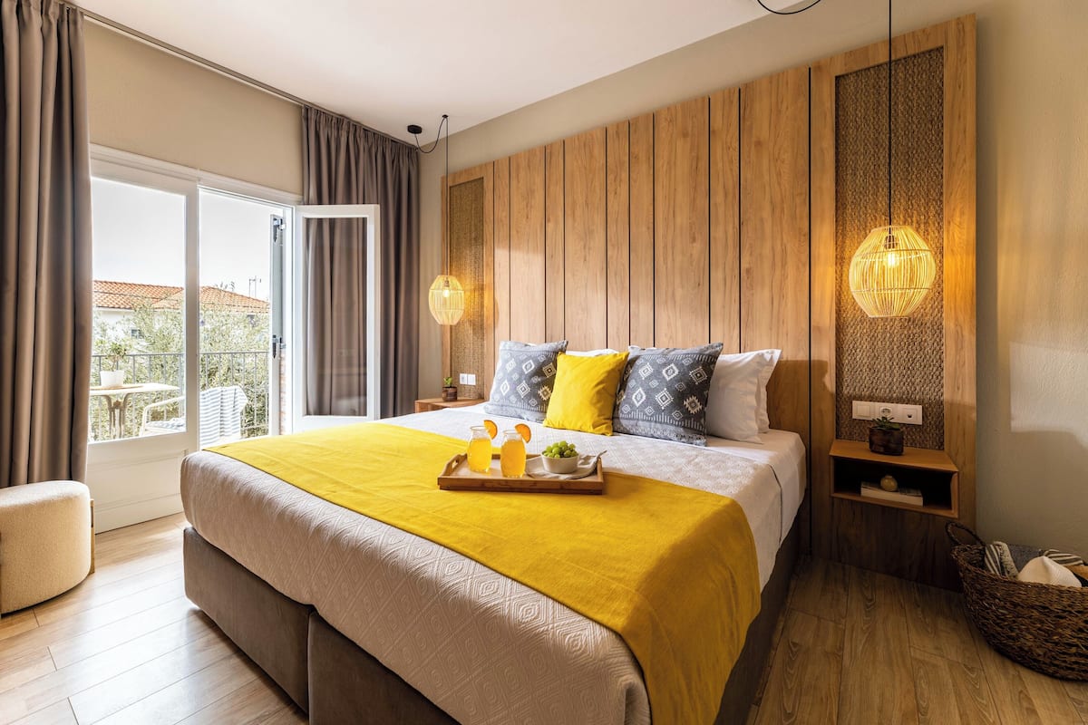 Habitación de hotel moderna con una cama grande, paneles de madera, un balcón y una colcha amarilla brillante.