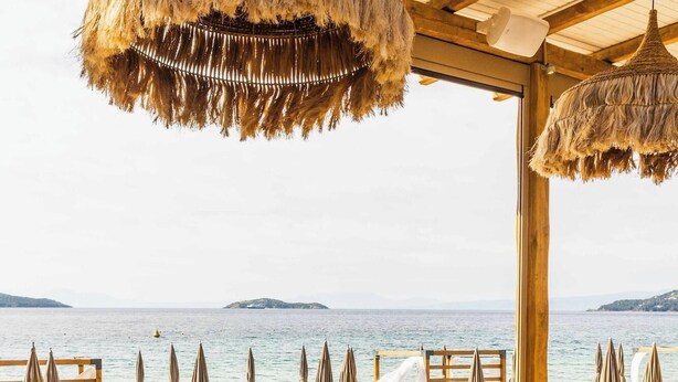 An outdoor dining area with a view of the sea, wooden furniture, and hanging thatch lamps. - Skiathos Thalassa (Skiathos)