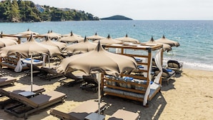 A beach with sun loungers and umbrellas, a wooden deck, and a view of the sea and a hill in the background. - Skiathos Thalassa (Skiathos)