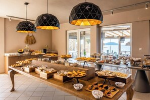 A buffet setup with various food items, geometric pendant lights, and a view of the sea. - Skiathos Thalassa (Skiathos)