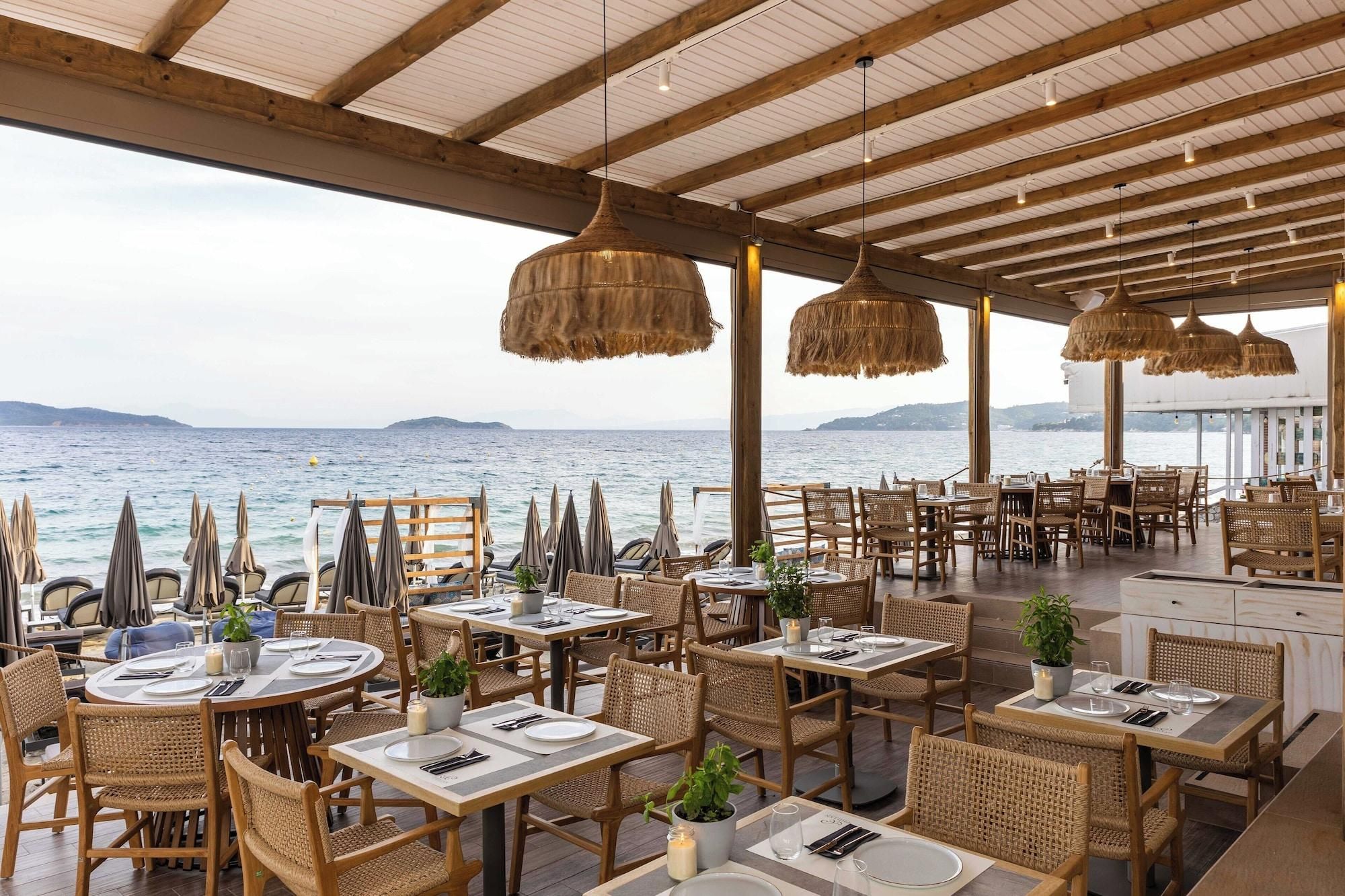 An outdoor restaurant with wicker furniture, tables set for dining, and a view of the sea.