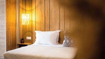 Una habitación de hotel con pared de paneles de madera, cama con ropa blanca, mesita de noche con lámpara y una planta pequeña.