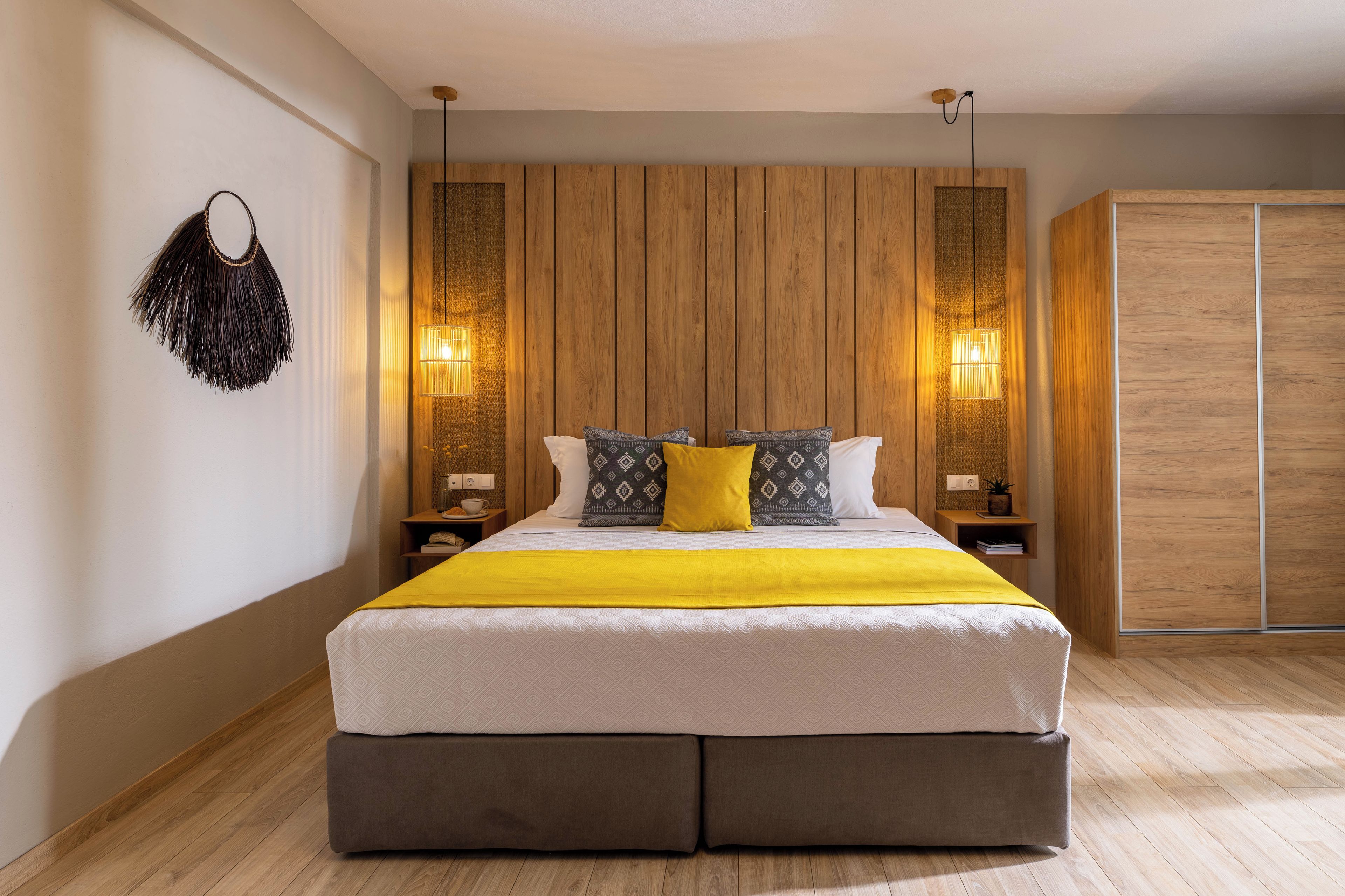 A modern bedroom with a large bed, wooden panel wall, bedside lamps, and a wardrobe.