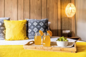 A bed with yellow bedding, two glasses of orange drink, a bowl of green grapes, and a wooden tray. - Skiathos Thalassa (Skiathos)