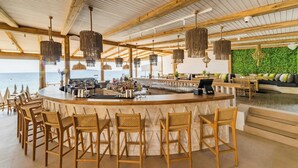 A bar area with a view of the ocean, wooden furniture, and hanging light fixtures. - Skiathos Thalassa (Skiathos)