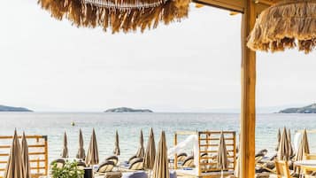 A dining area with a view of the sea, wooden furniture, and hanging thatched lamps.