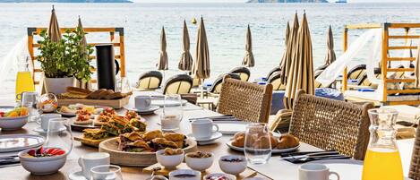 A table set for breakfast with various dishes, drinks, and a view of the sea.
