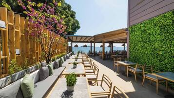 Un espacio de comedor al aire libre con mesas y sillas, cerca de una valla de madera y una pared verde.