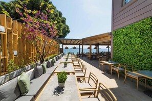 An outdoor dining area with tables and chairs, a wooden fence, and a green wall. - Skiathos Thalassa (Skiathos)