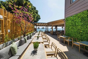 Un espacio de comedor al aire libre con mesas y sillas, cerca de una valla de madera y una pared verde.