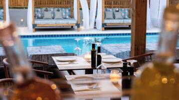 A dining area with a pool view, wooden furniture, and candles.