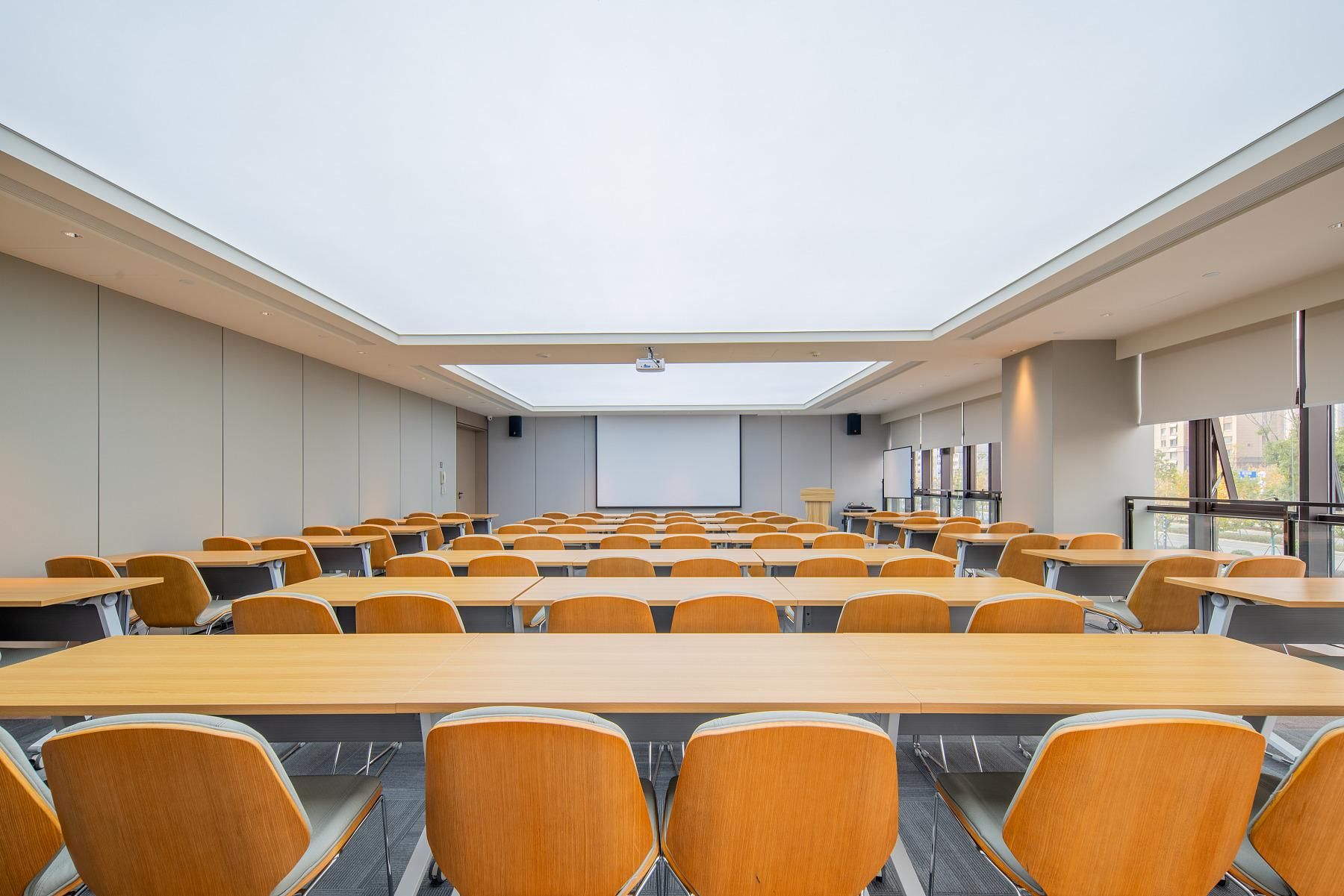 A conference room with a high ceiling, skylight, and rows of wooden tables and chairs.
