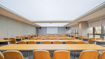 A conference room with a high ceiling, skylight, and rows of wooden tables and chairs.